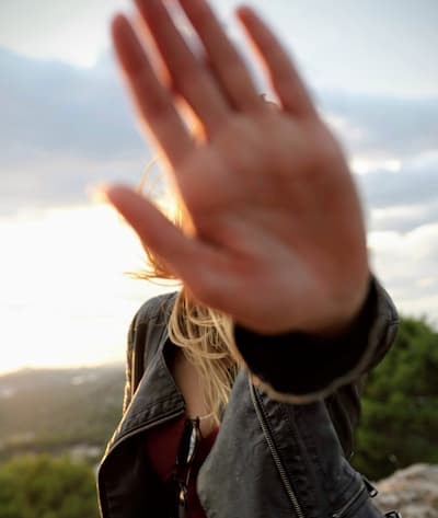 Young person putting their hand up to the camera to hide their face